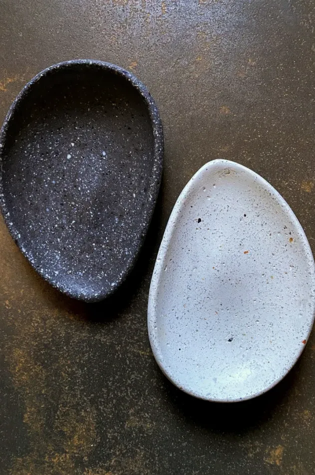 Due ciotole a goccia, scura e chiara, su una superficie bronzo