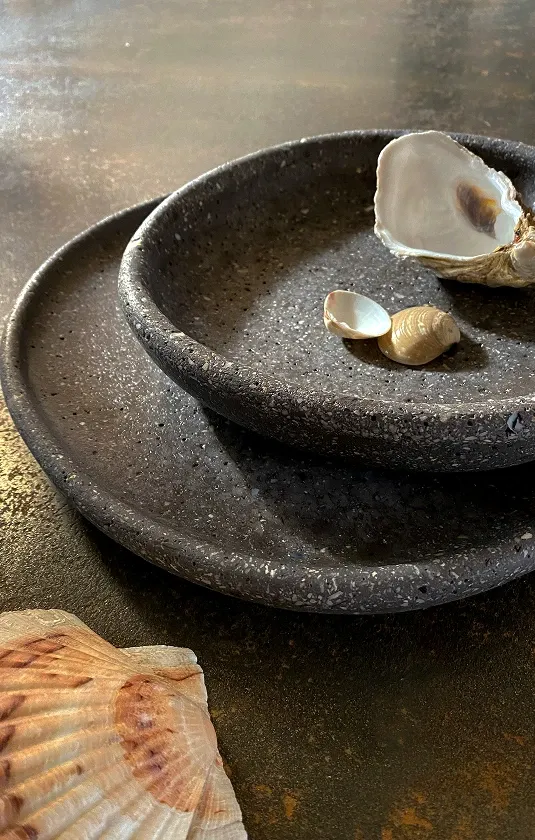 Collezione Mareggiata: piatti scuri sovrapposti con conchiglie
